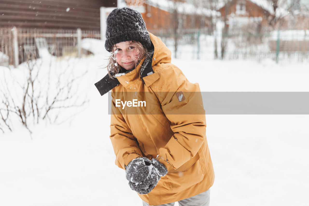 Girl in plays in backyard and enjoys sunny day in winter, she stands on snowdrift 