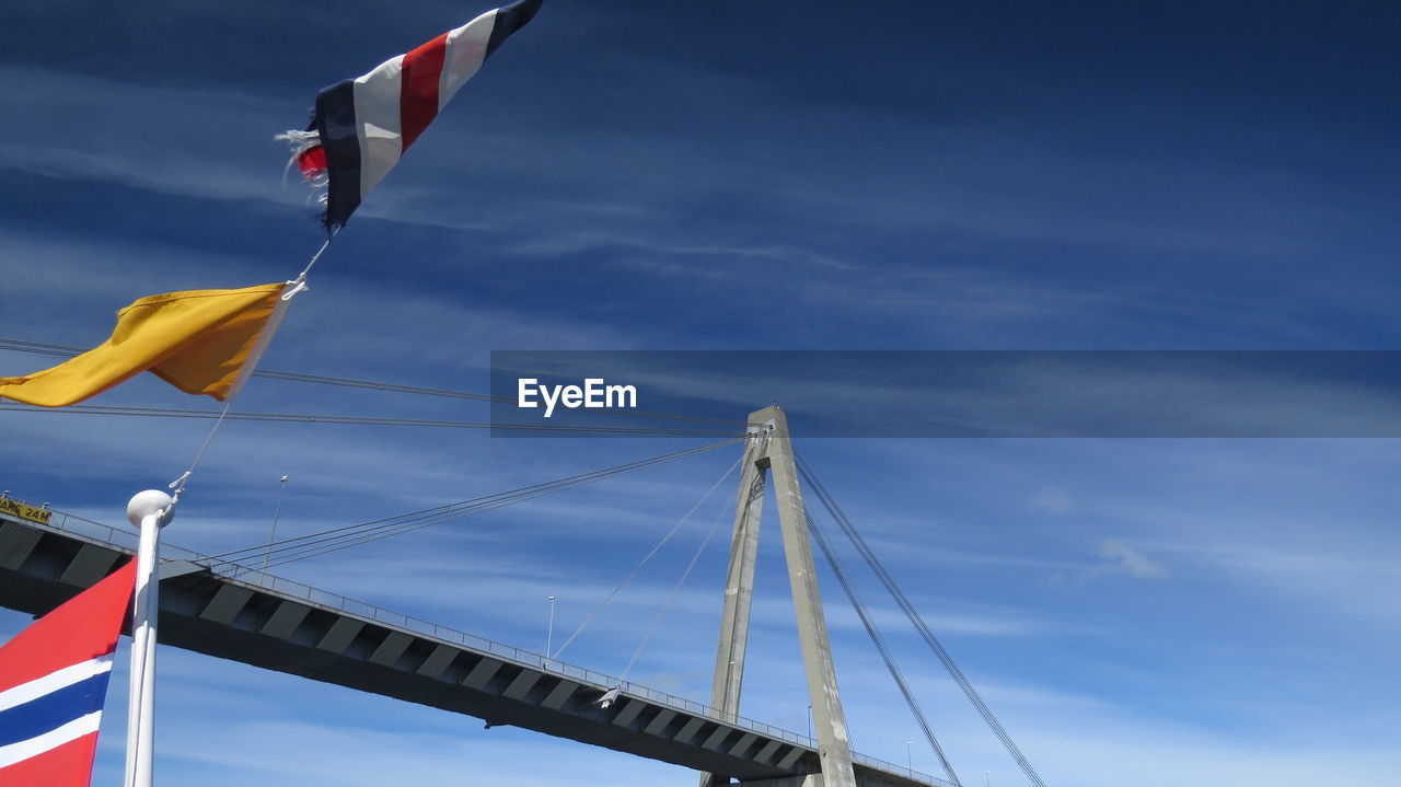 Low angle view of flags and bridge against blue sky