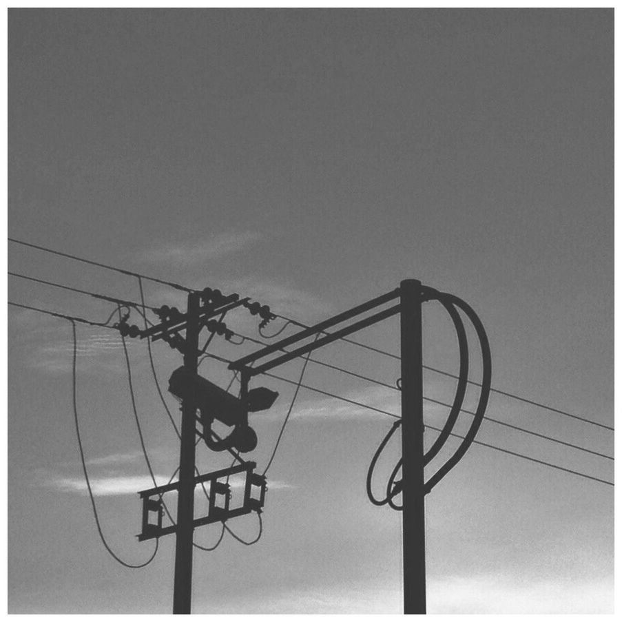 Low angle view of silhouette electricity pylons against sky