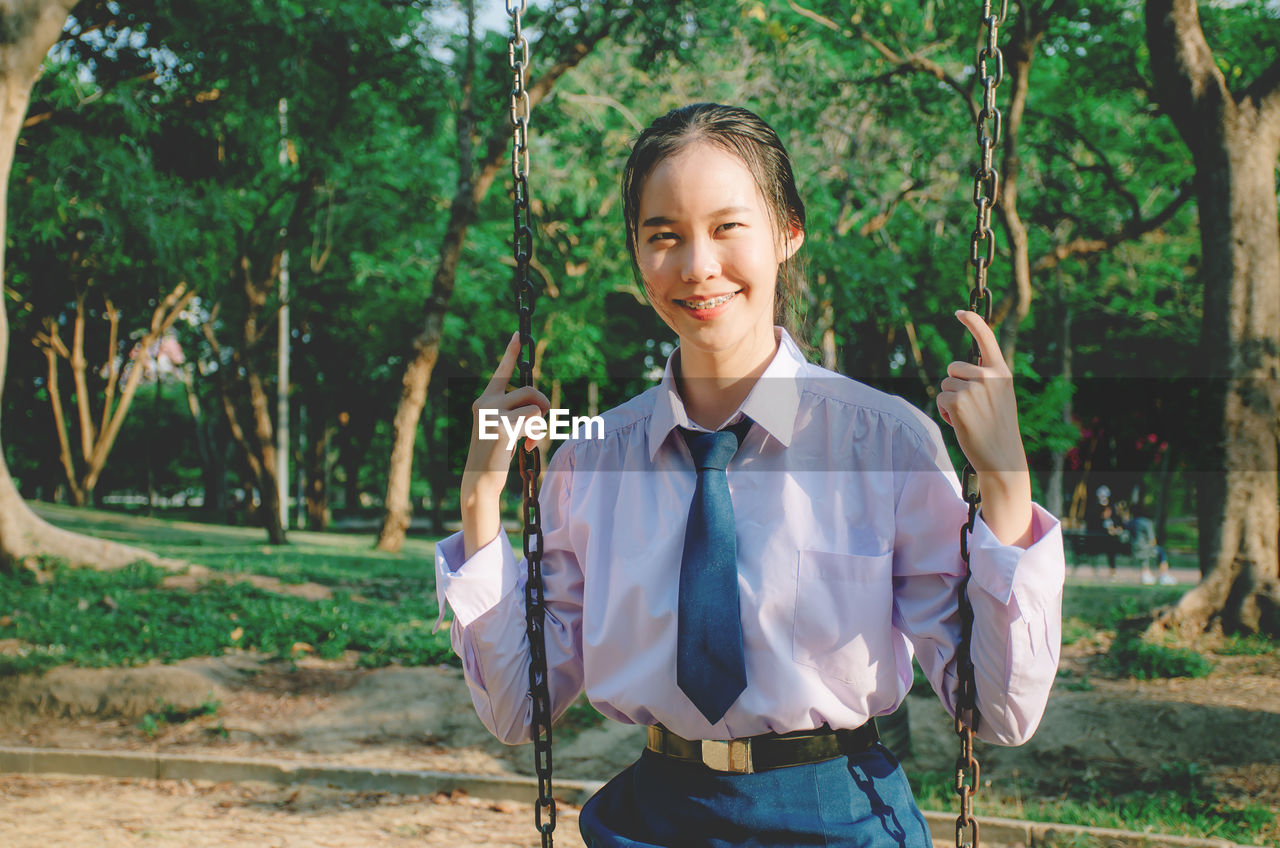 PORTRAIT OF SMILING YOUNG WOMAN STANDING BY TREE