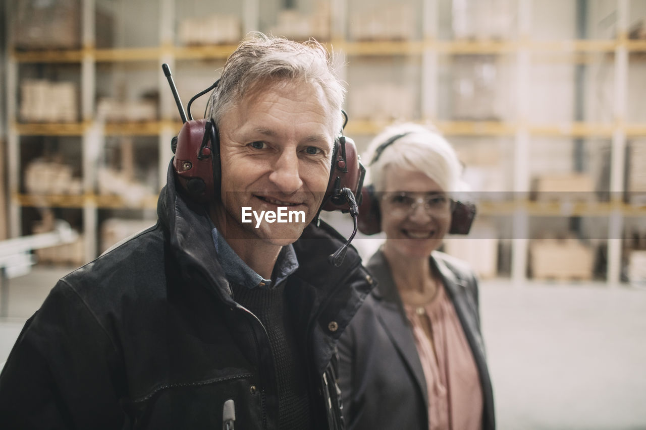 Portrait of smiling businessman with colleague wearing ear protectors at industry