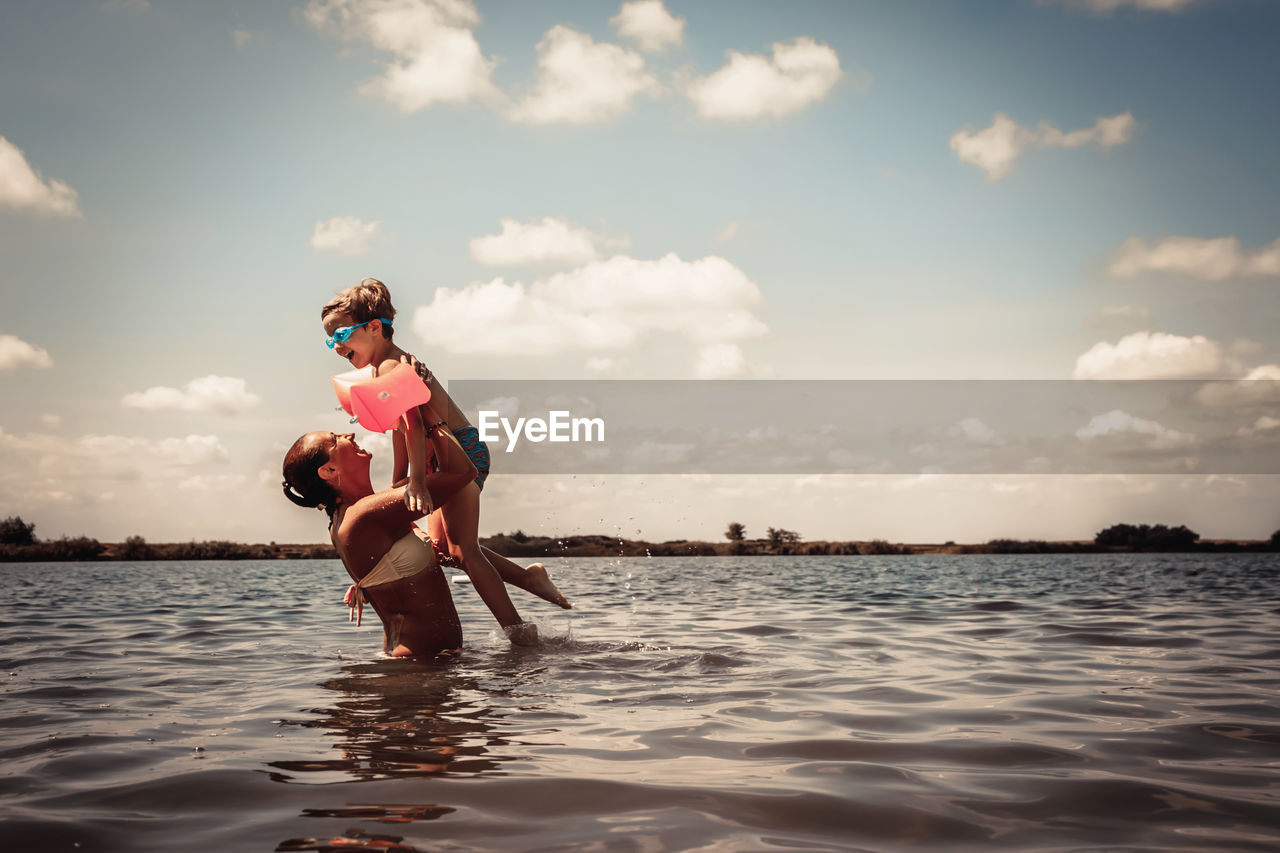 Cheerful mother and son having fun in the water in summer day.