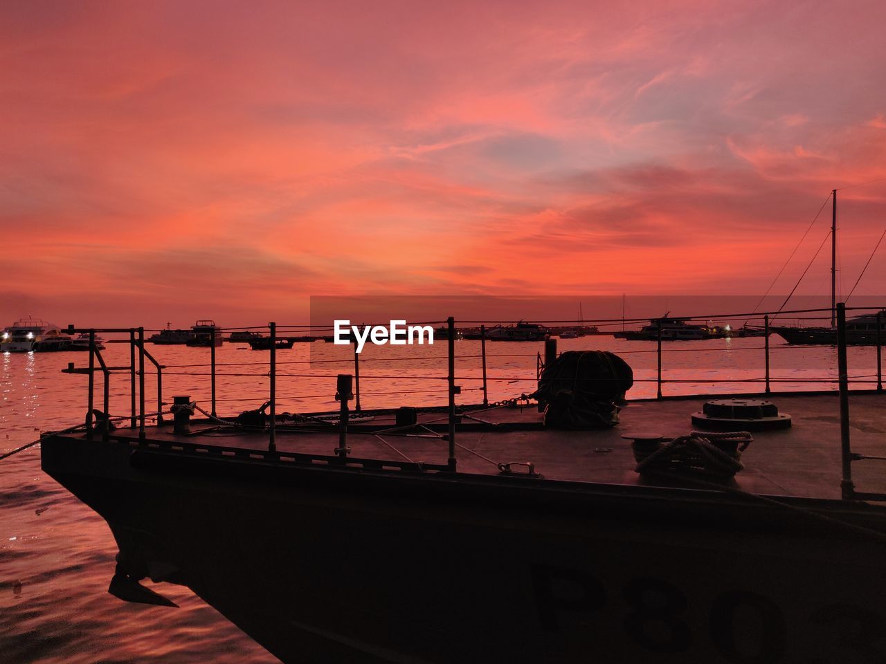 Silhouette boats moored in sea against orange sky