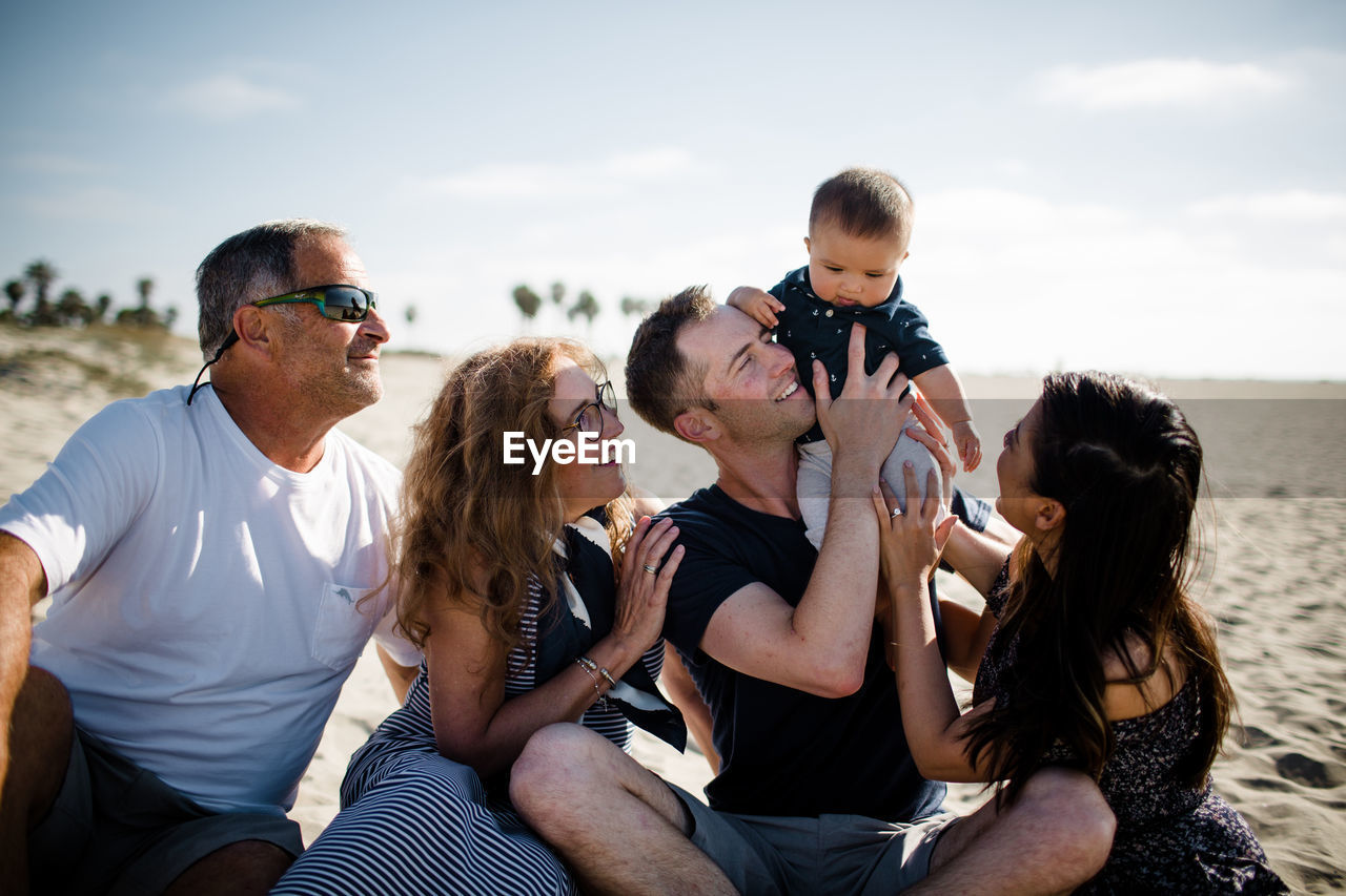 Family of five sitting on beach smiling at infant