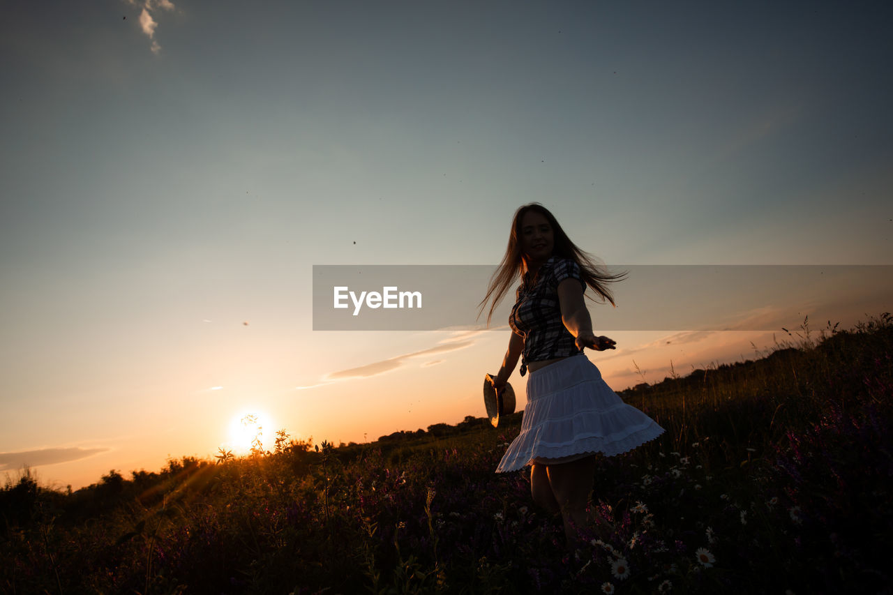 WOMAN WITH UMBRELLA ON FIELD AT SUNSET