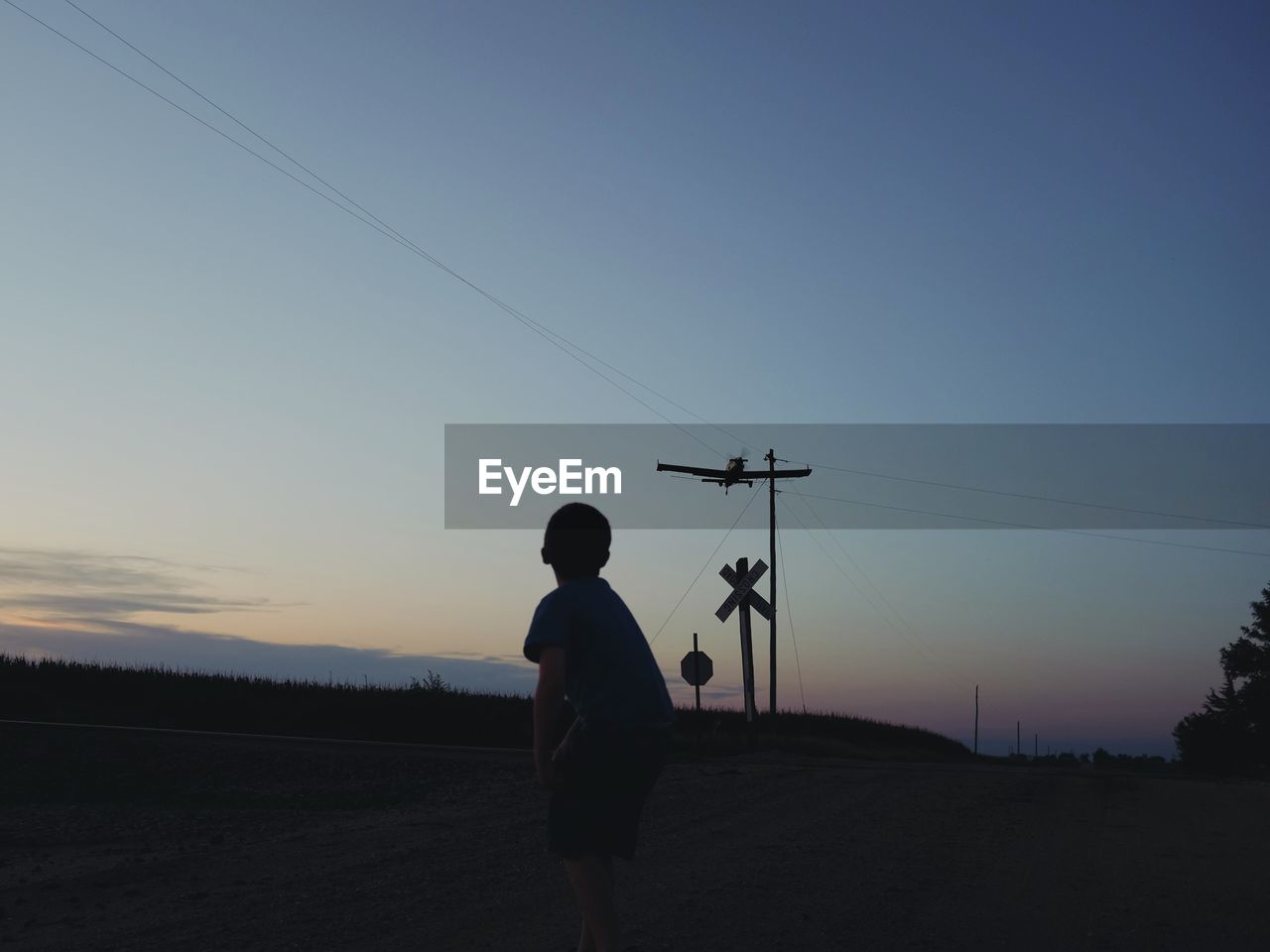 Boy looking at airplane flying in sky during sunset