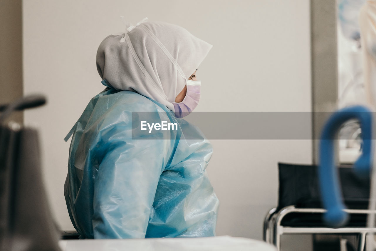 Side view of woman wearing mask and sitting on chair in hospital
