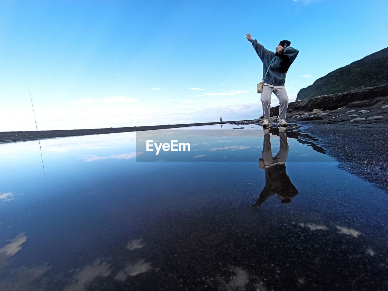 water, sea, one person, reflection, sky, nature, adult, full length, blue, environment, ocean, beauty in nature, men, scenics - nature, horizon, tranquility, limb, standing, land, mountain, day, leisure activity, travel, coast, holiday, outdoors, landscape, person, vacation, footwear, trip, tranquil scene, arm, lifestyles, young adult, human limb, activity, beach, sunlight