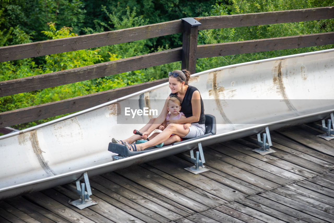 SIDE VIEW OF WOMAN SITTING ON RAILING BY BRIDGE
