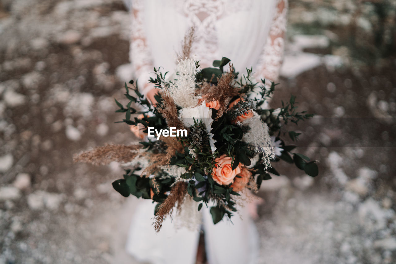 Crop anonymous female bride with delicate flower blooming bouquet wearing elegant white dress