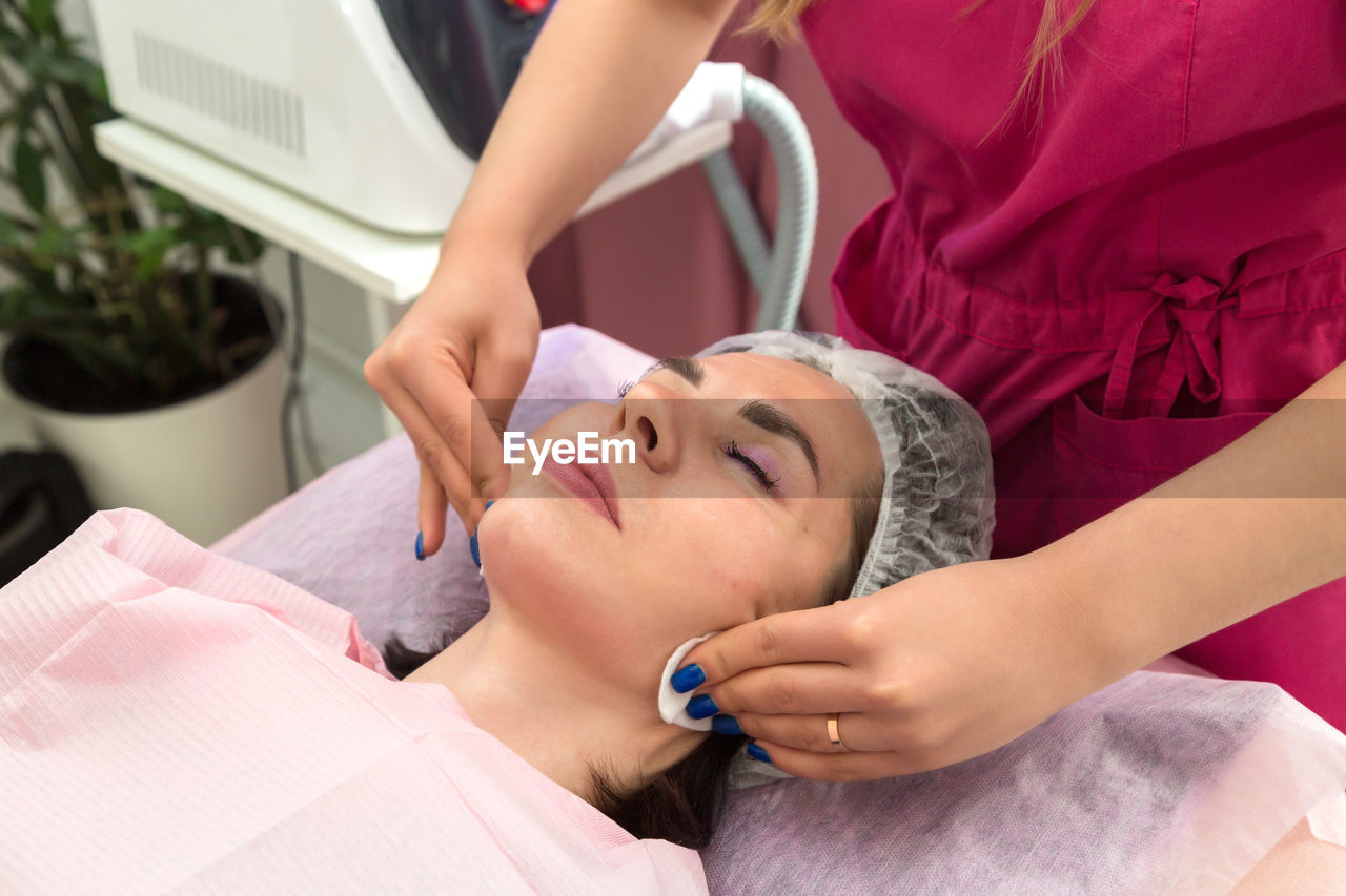 An adult woman is wiped with a cotton pad after the carbon peeling procedure in a beauty salon.