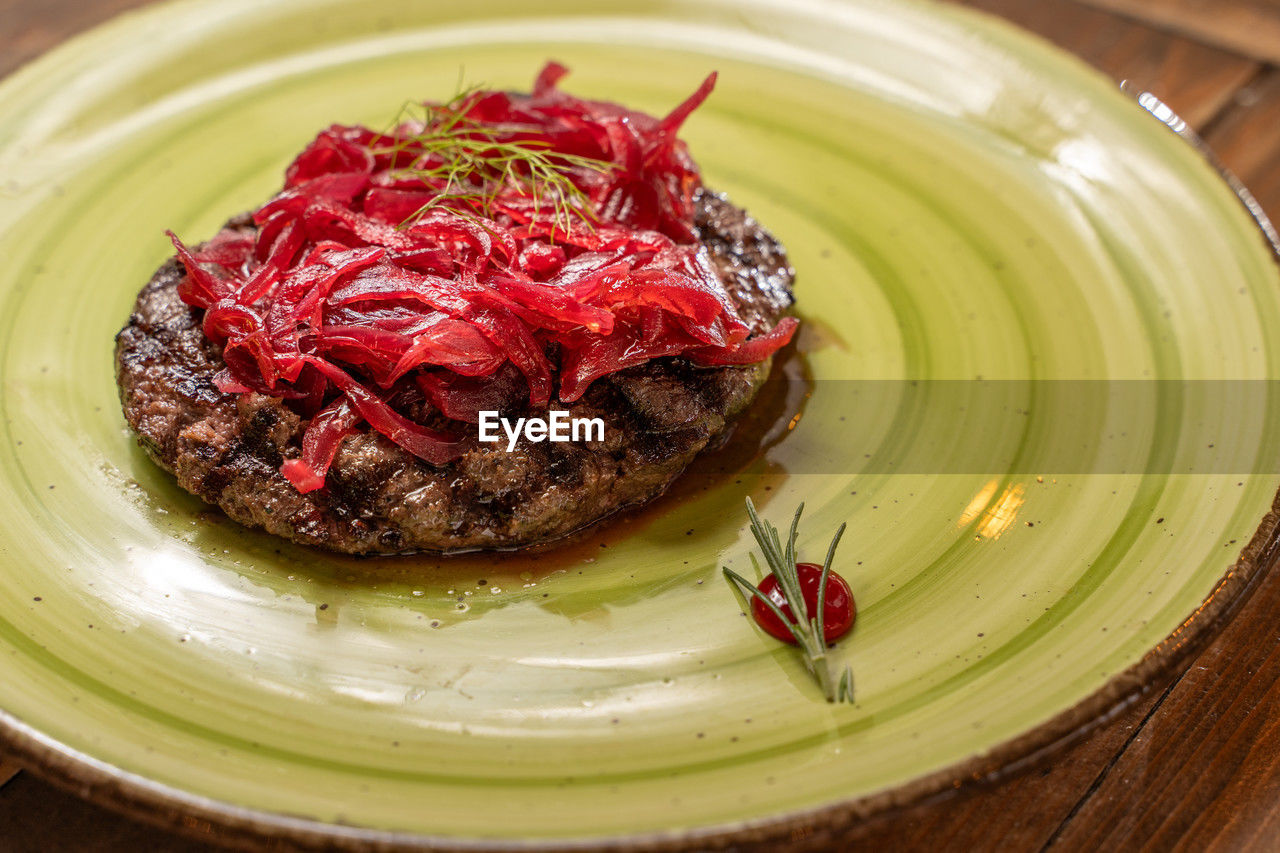 Gourmet burger served on a green plate with caramelized red onions and herbs.