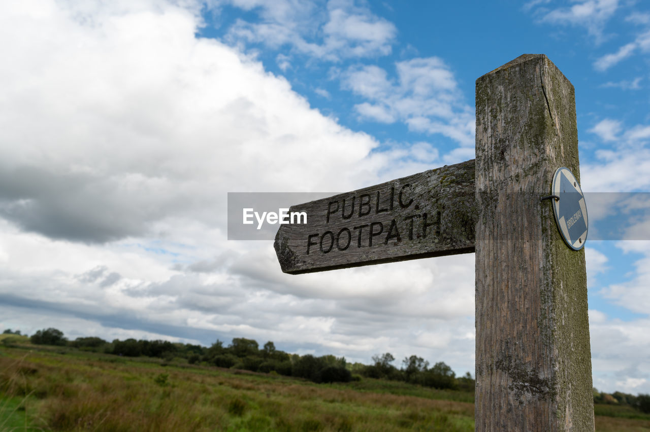 SIGN BOARD ON WOODEN POST AGAINST SKY