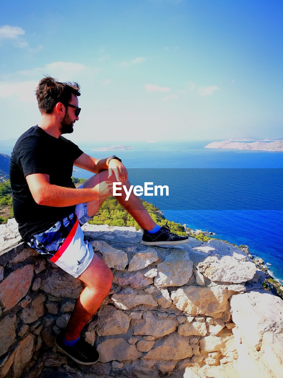 Side view of man sitting at observation point against sea