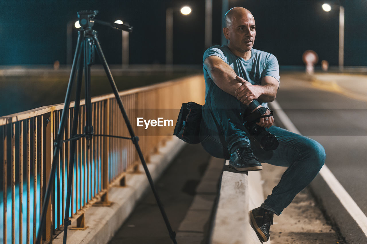 Man holding camera sitting by railing at night