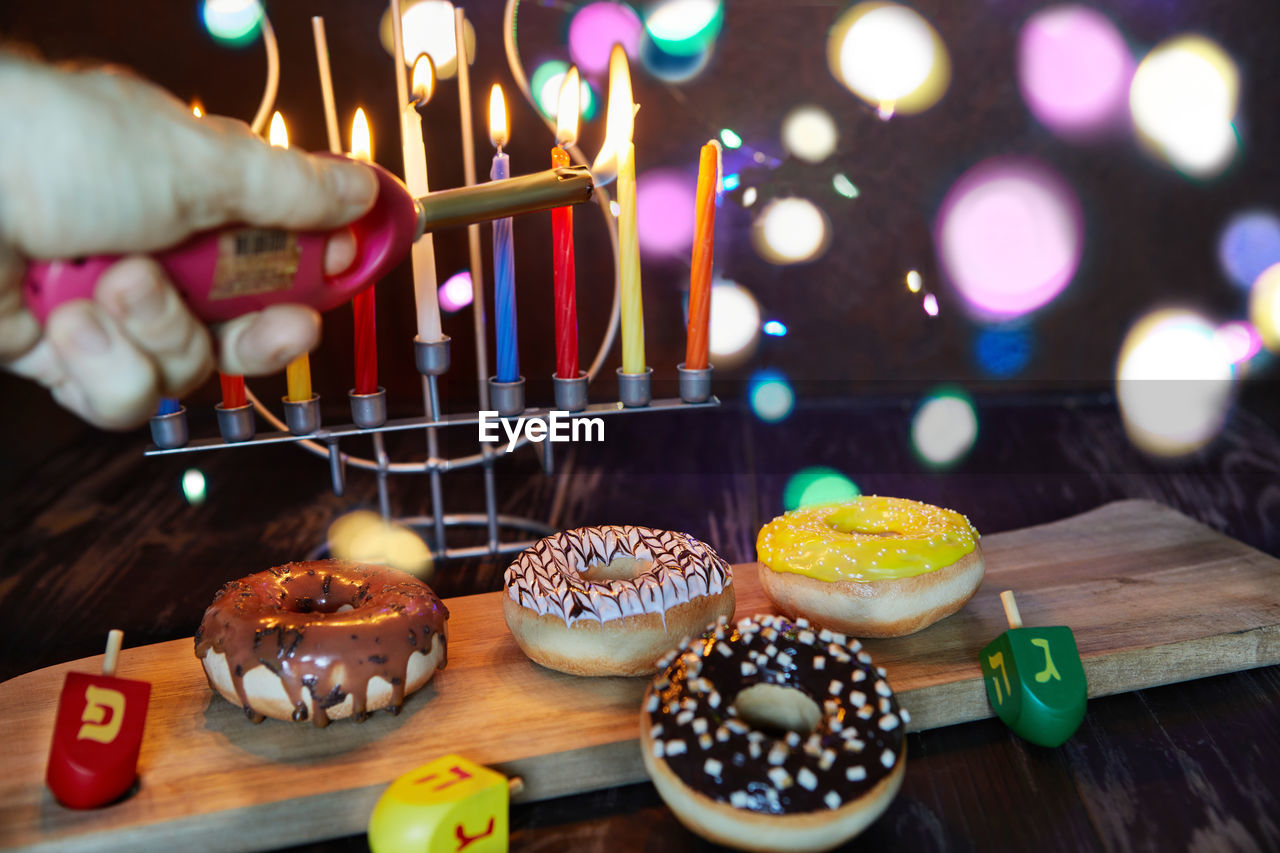  traditional jewish candlestick with candles, donuts and spinning tops on brown wooden background