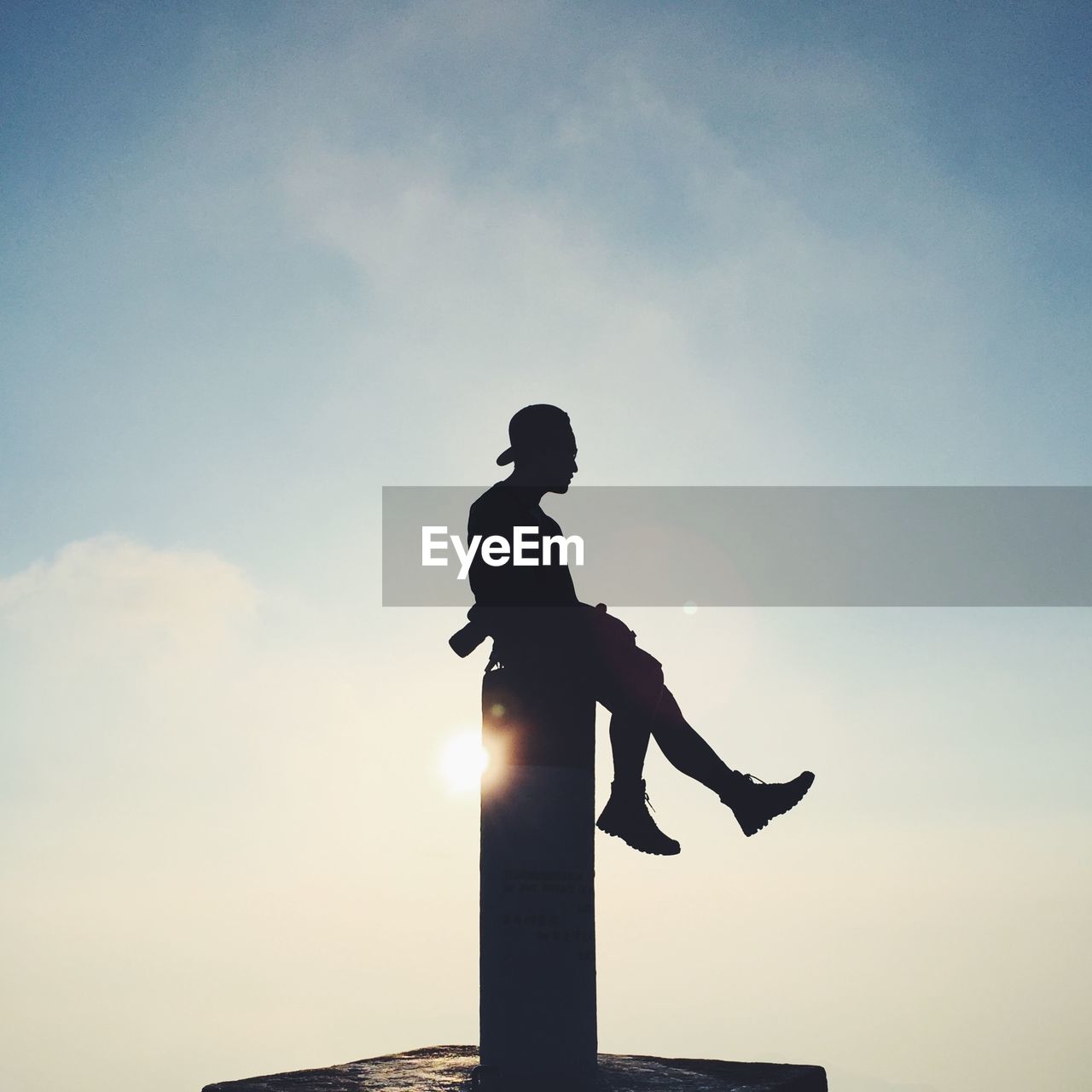 Silhouette man sitting on pole against sky during sunset