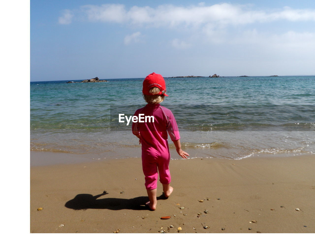 Rear view of child walking towards sea shore against sky
