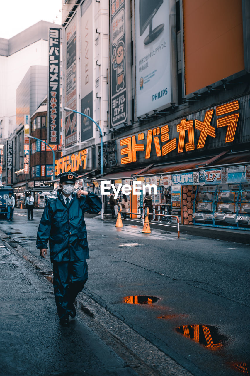 Man in uniform walking on road by buildings in city