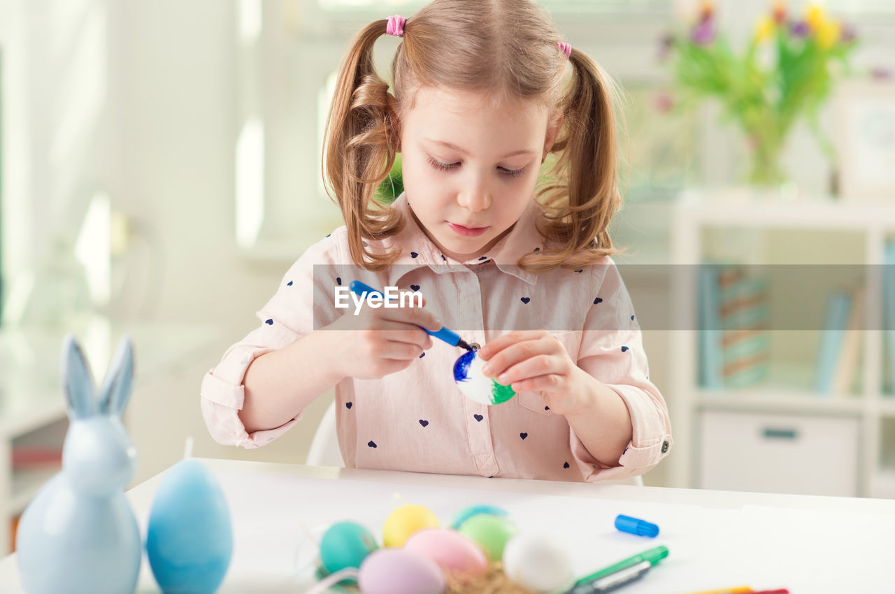 Cute girl painting easter egg while sitting at home