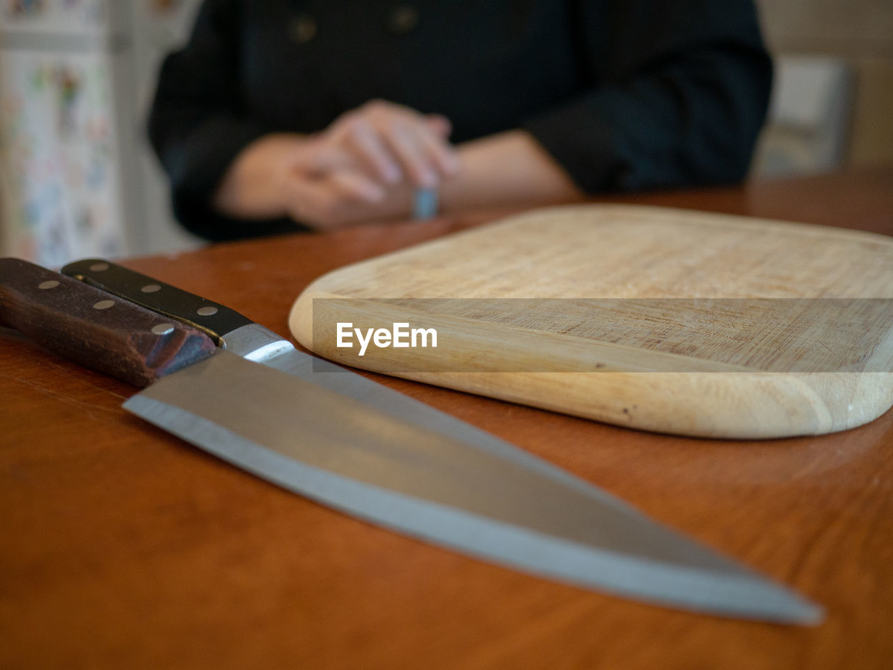 Midsection of person with cutting board and knives on table