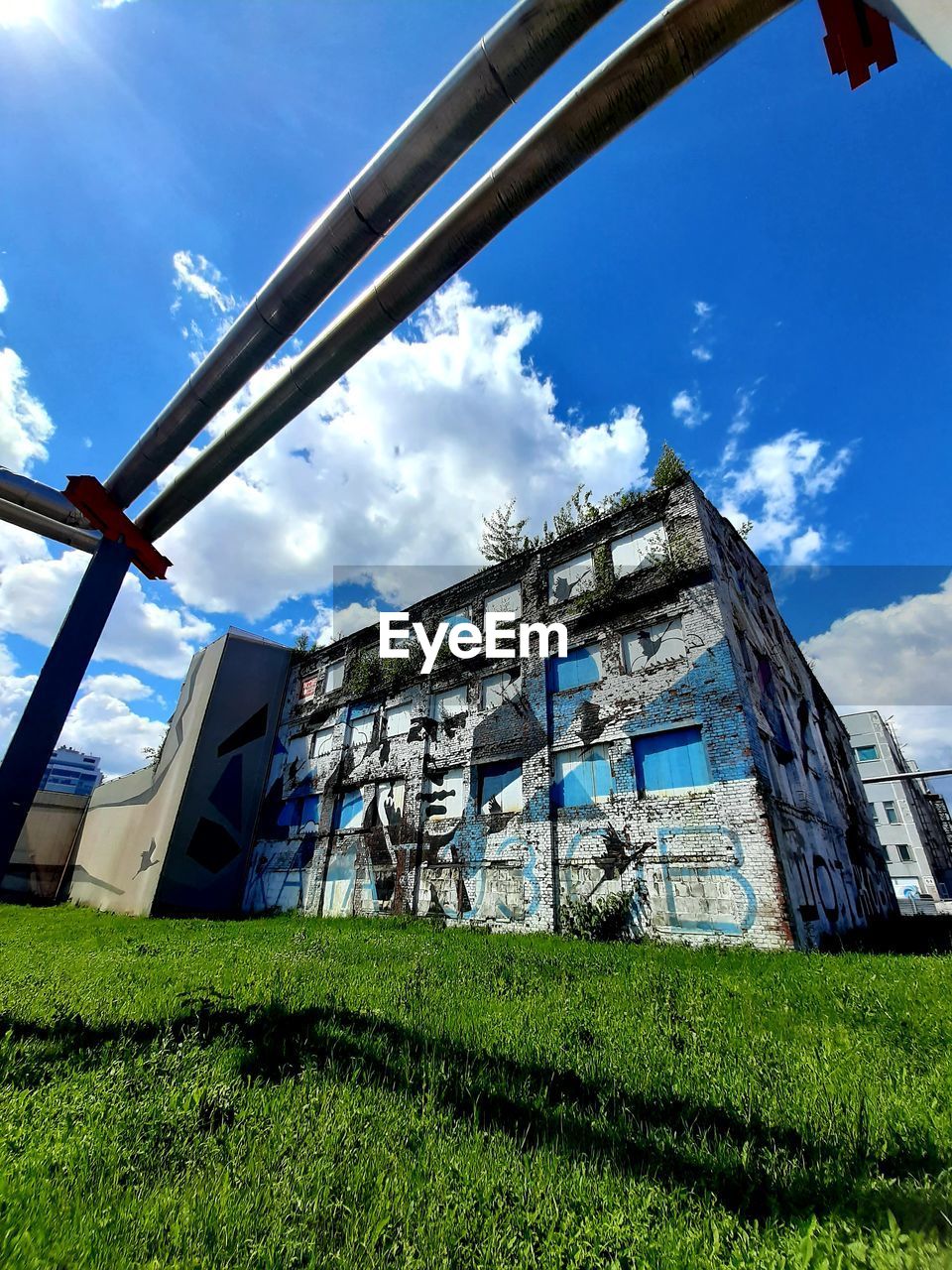 sky, architecture, grass, built structure, cloud, nature, plant, building exterior, urban area, no people, day, stadium, building, blue, low angle view, outdoors, industry, sunlight, landmark, sport venue, green