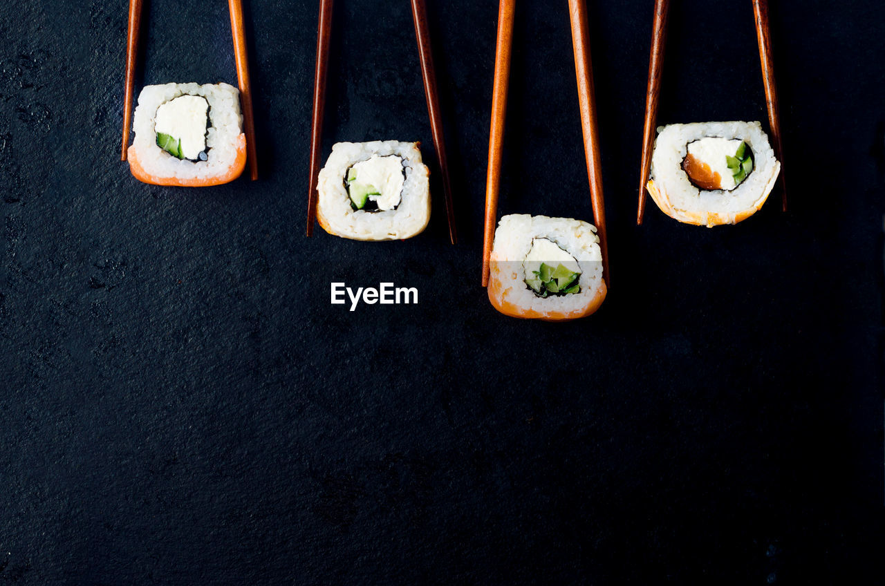 Fresh tasty sushi with salmon in wooden chopsticks on a dark background. 