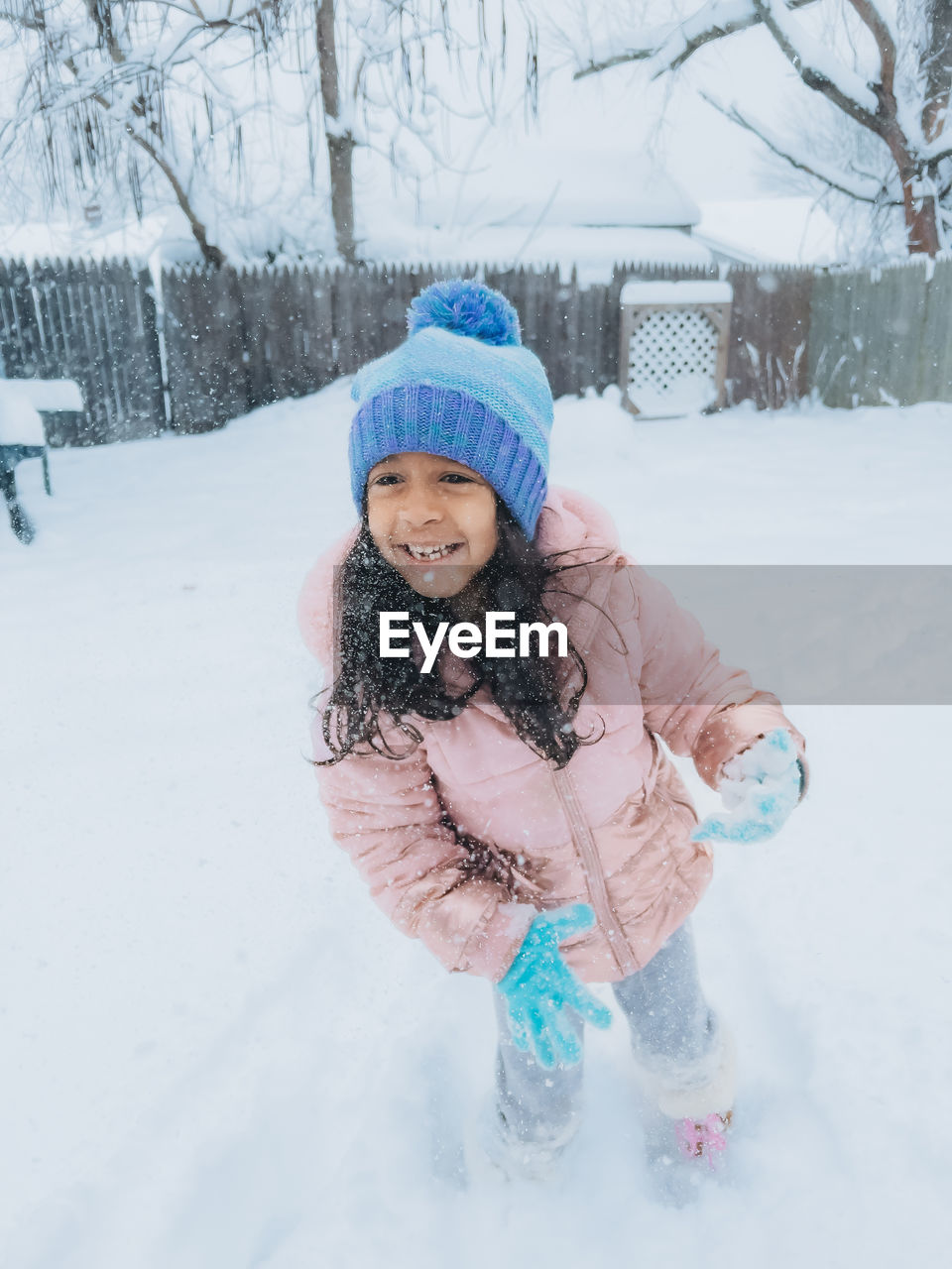 Diverse mixed race pre school toddler girl outdoors in winter playing with snow 