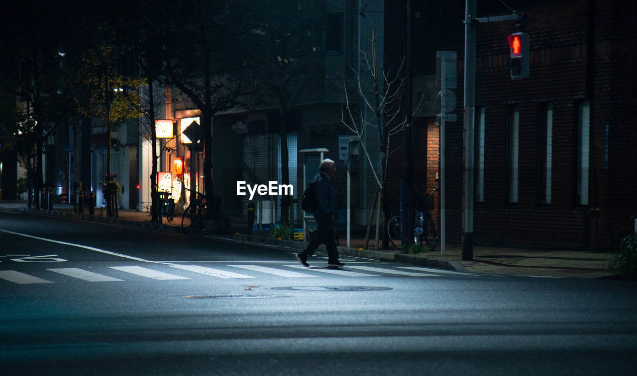 MAN WALKING ON ILLUMINATED CITY STREET