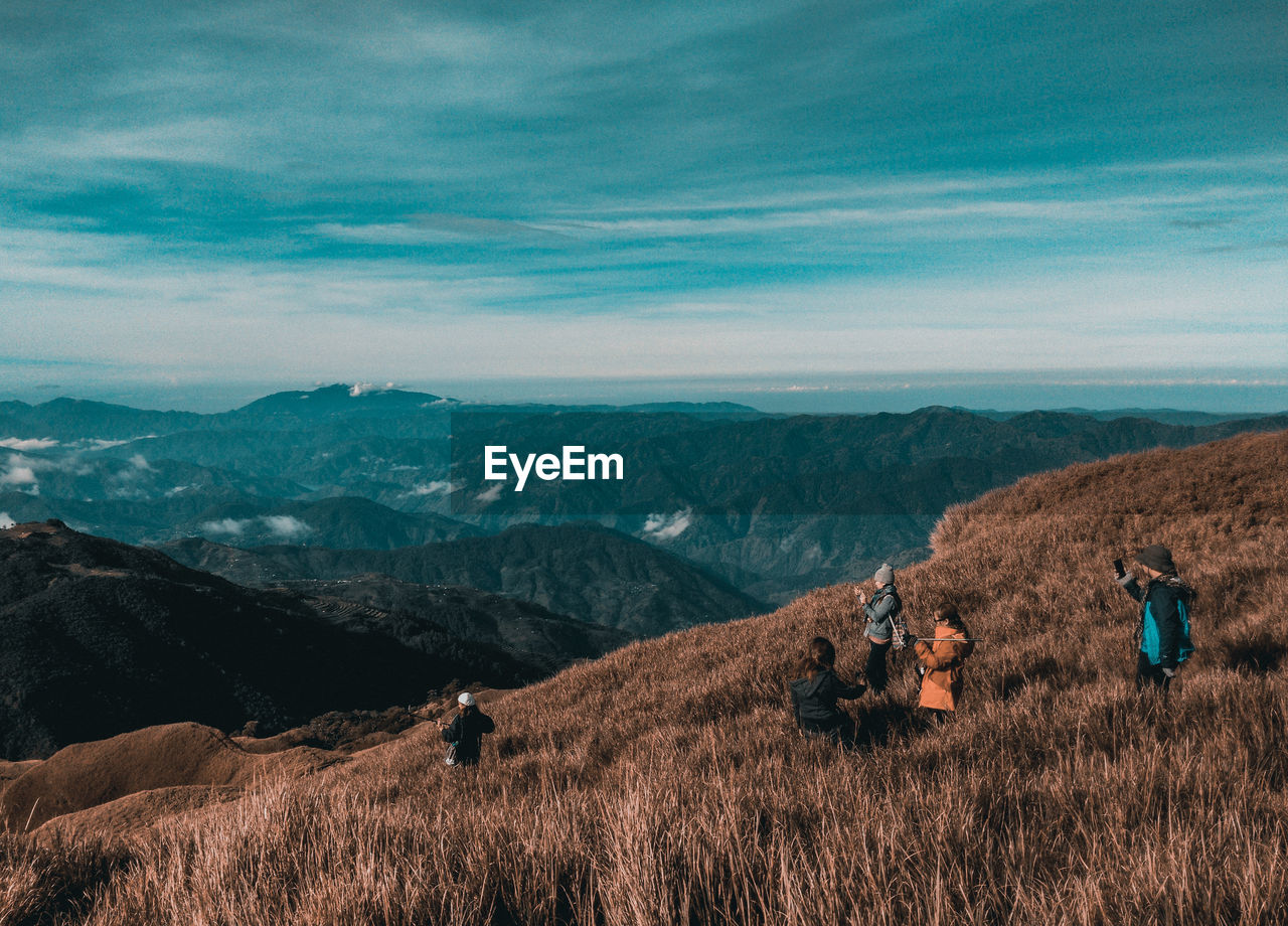 People photographing on field by mountains against cloudy sky