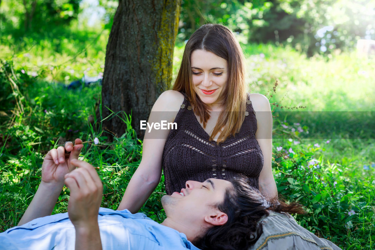 YOUNG WOMAN SMILING WHILE SITTING ON GRASS