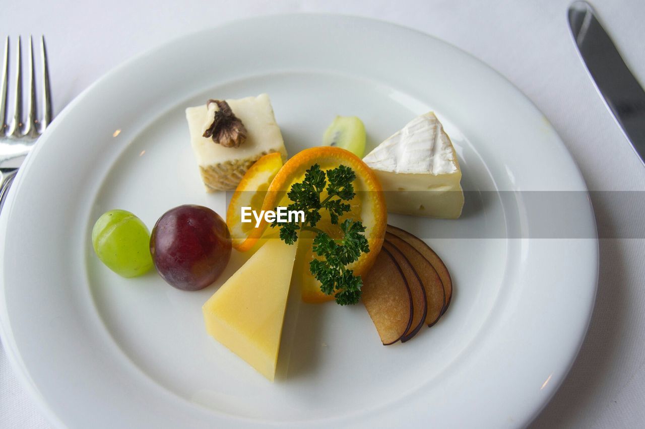 High angle view of cheese and fruits in plate on table