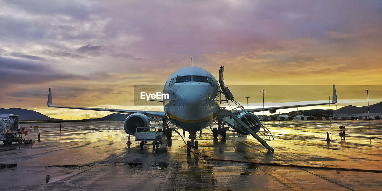 Airplane on runway against sky during sunset