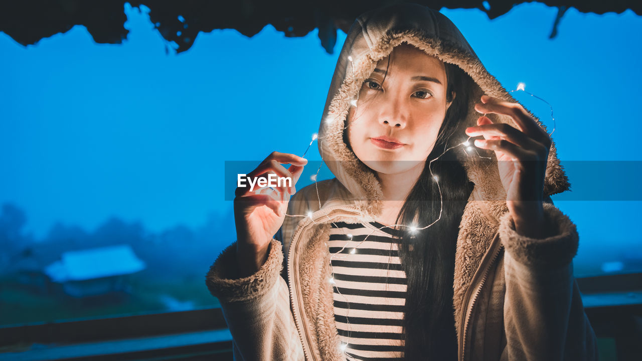 Portrait of woman holding illuminated string lights at night