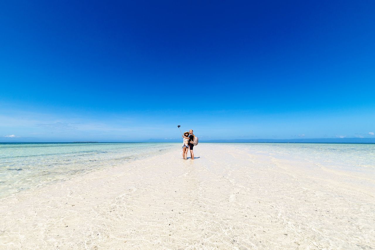 View of couple on beach against clear blue sky