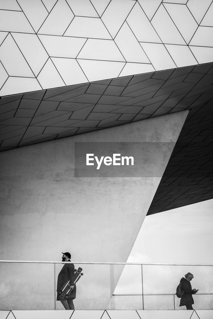 LOW ANGLE VIEW OF MAN WALKING AGAINST BUILDING