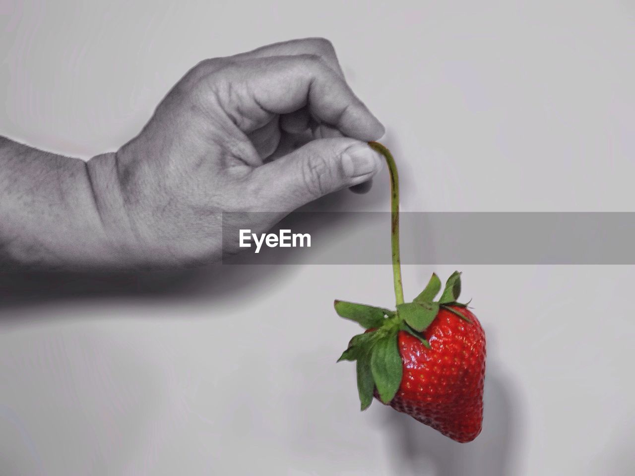 Cropped image of person holding strawberry against white background