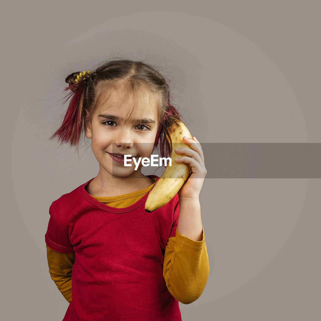 PORTRAIT OF SMILING GIRL HOLDING ICE CREAM AGAINST GRAY BACKGROUND