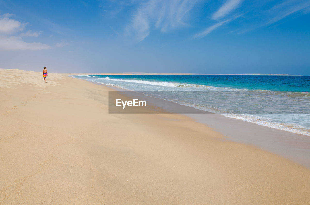 Scenic view of woman walking on empty beach against sky