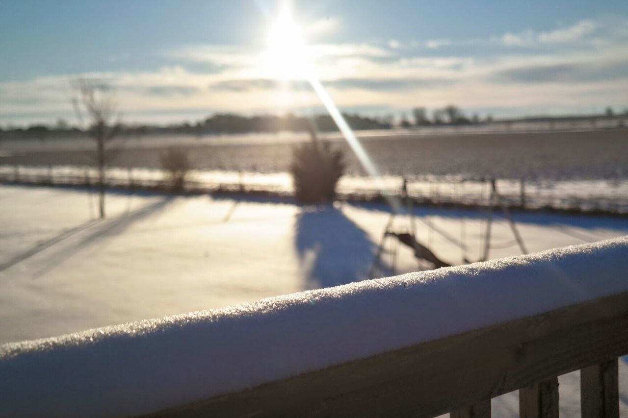 Snow covered railing on field against bright sun