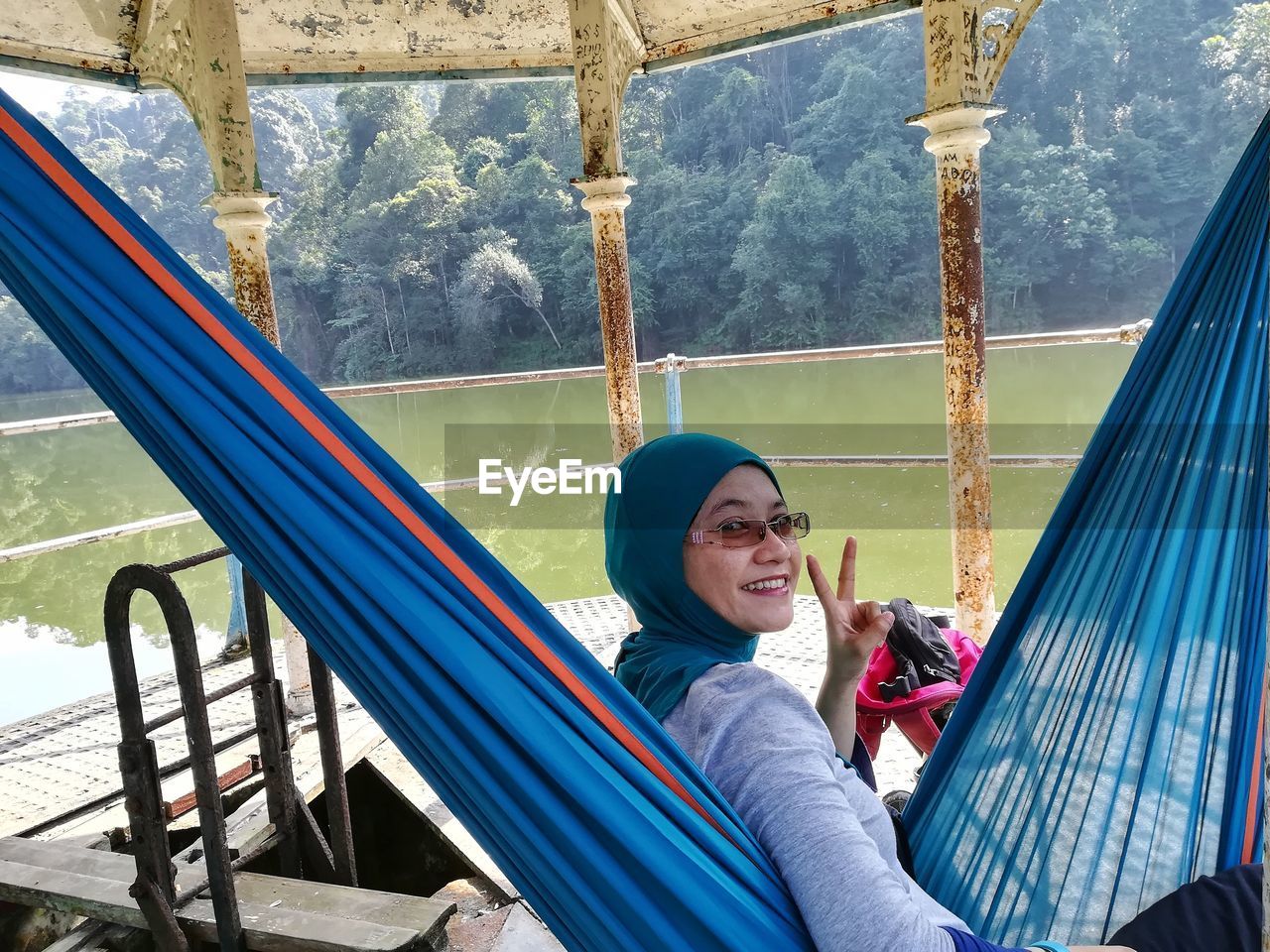 Portrait of smiling woman showing peace sign while relaxing on hammock