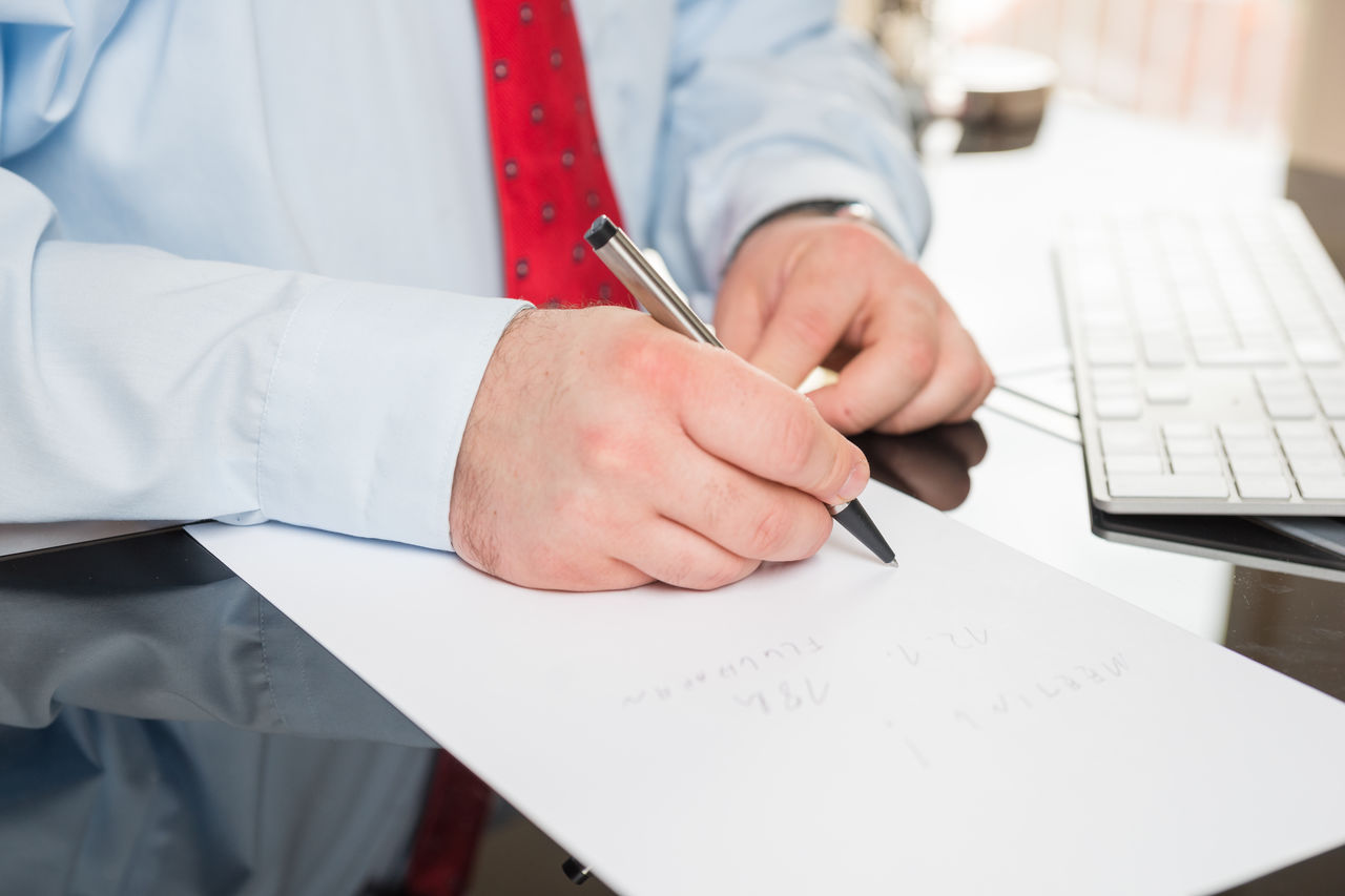 Midsection of businessman writing on paper at desk in office