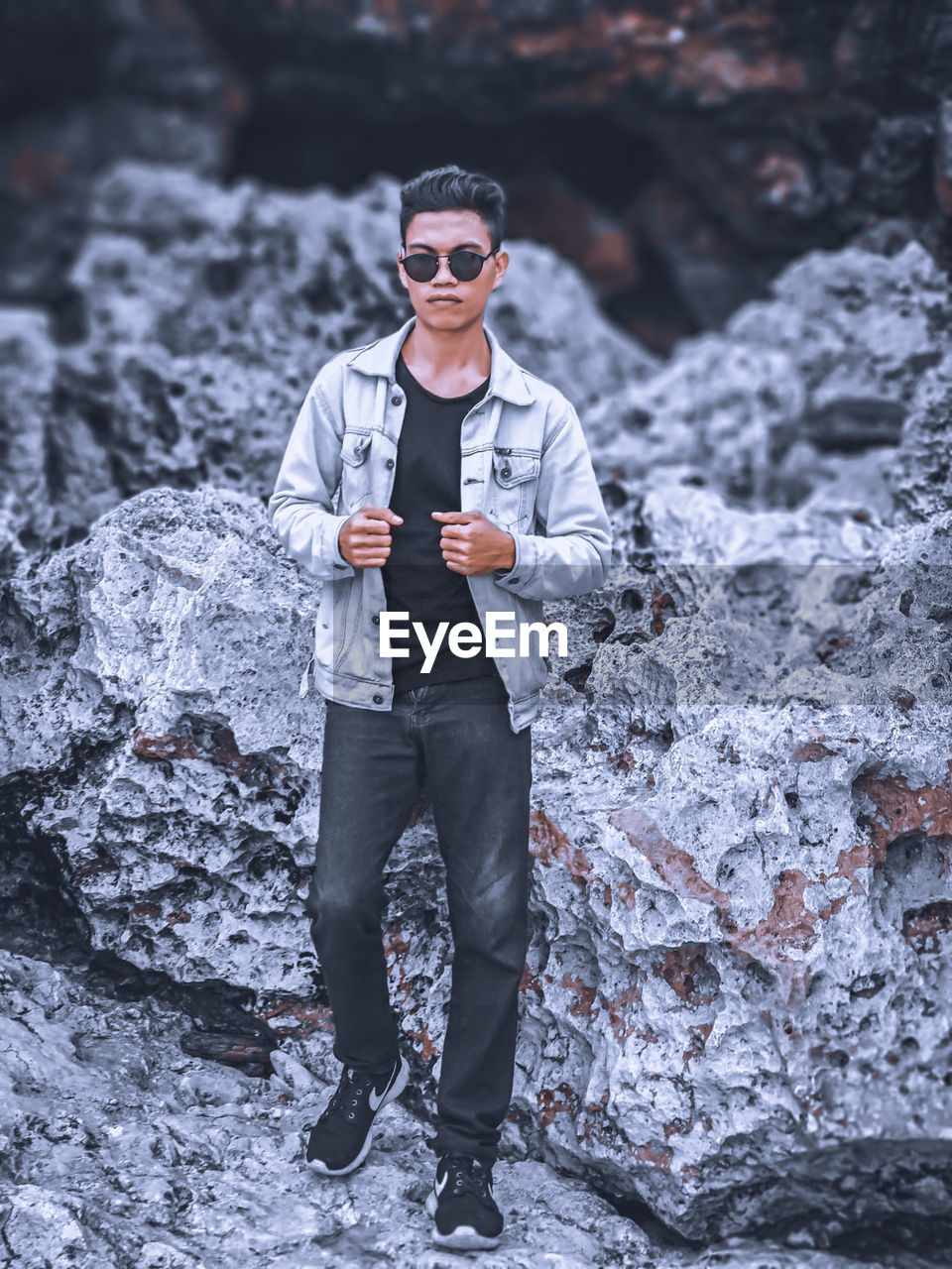 PORTRAIT OF YOUNG MAN STANDING BY ROCK