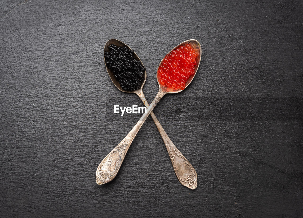 Grainy caviar of paddlefish fish and red chum salmon caviar in a spoon, black background, top view