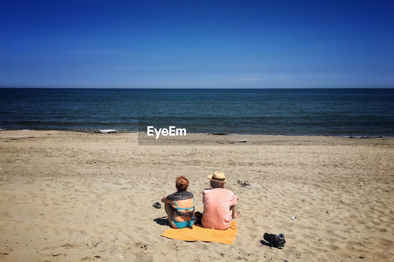 REAR VIEW OF FRIENDS SITTING ON BEACH