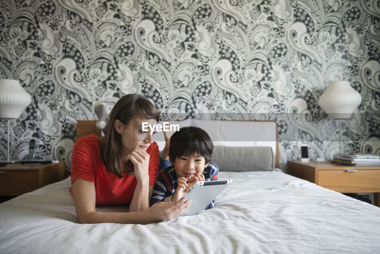 Mother and son using digital tablet while lying on bed