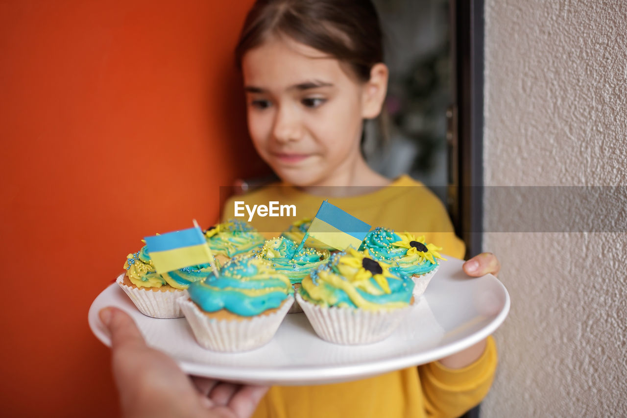 Ukrainian girl for whom neighbors brought cupcakes with cream in yellow and blue colors for brunch