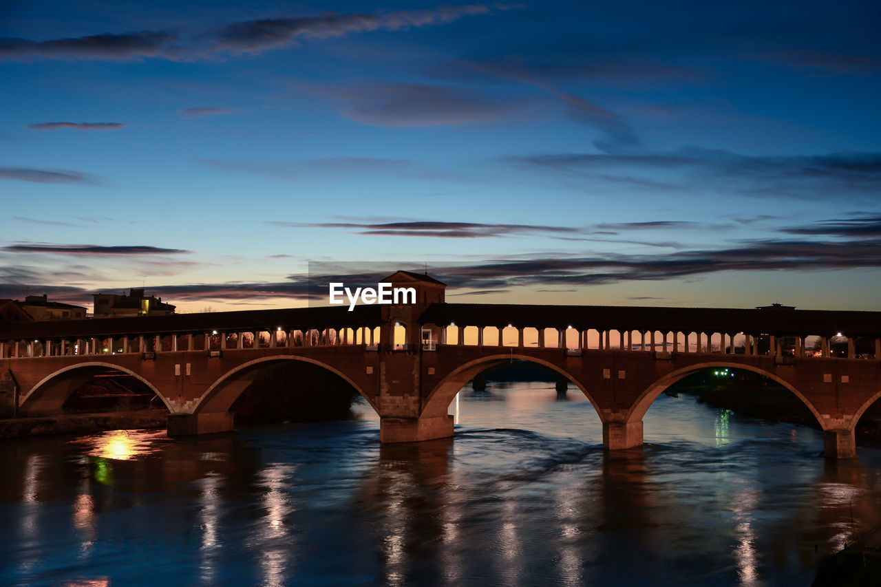 Arch bridge over river against sky at sunset