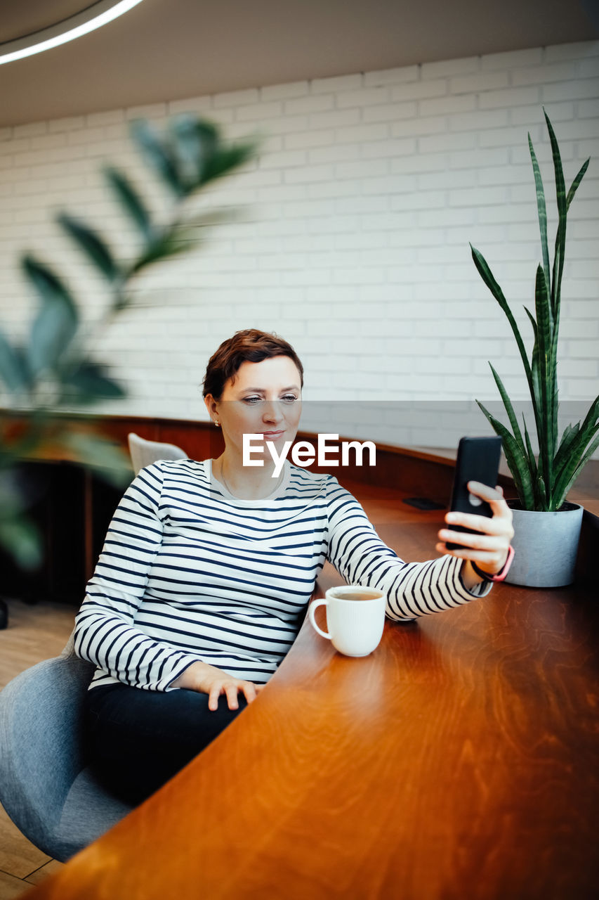 A woman sits at a table in a modern office and communicates on a smartphone