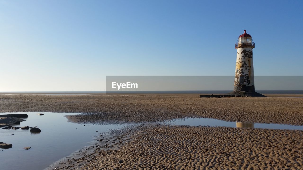 Lighthouse at beach against clear sky